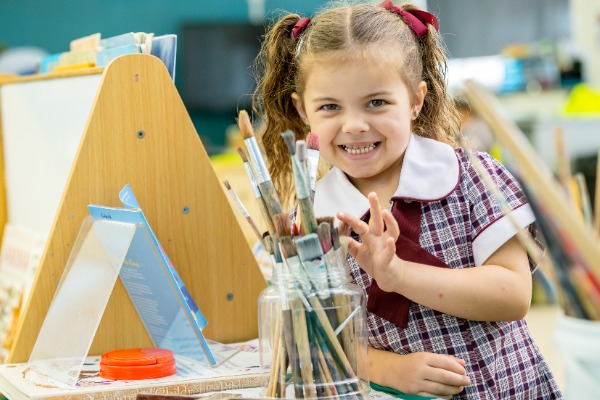 Prep student inside at a painting easel with paint brushes
